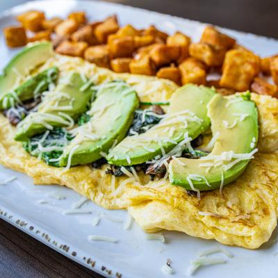 Spinach Mushroom Omelet topped with avocado slices, with home fries.