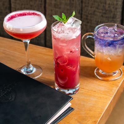 Three different cocktails served on a table beside a menu.