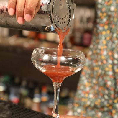 A cocktail being poured into a coupe glass.