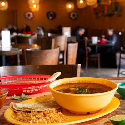 A bowl of Mexican meatballs in tomato broth with vegetables, served with rice and tortilla chips.