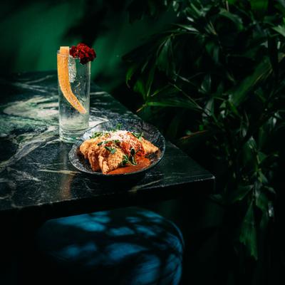 Empanadas and a cocktail on a table against a leafy backdrop.