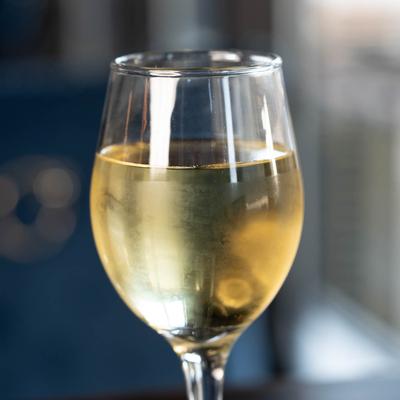 A glass of white wine sits on a table with a blurred background, close up.