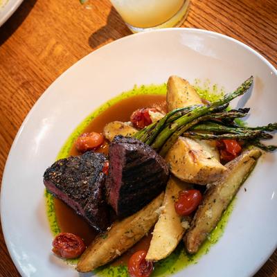 A hanger steak served with roasted potato, asparagus, and cherry tomatoes.