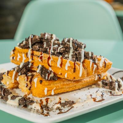 Churros topped with crushed cookies and drizzled chocolate and cream.