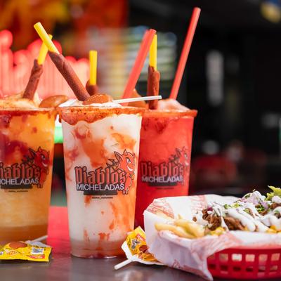 Three flavored margaritas in branded cups beside a basket of loaded fries.