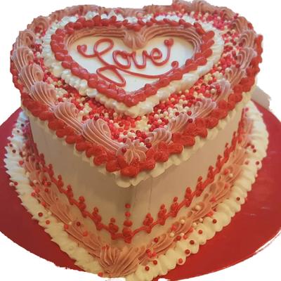 Heart-shaped cake decorated in white, pink, and red icing with Love written on top.