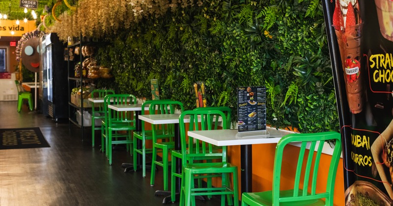 Café interior with green foliage walls, green chairs, white tables, hanging floral decor