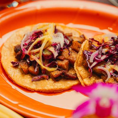 Pork belly tacos with cabbage topping on an orange plate.