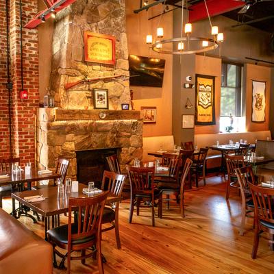 Dining space featuring a large stone fireplace, wooden floors, booths and tables.