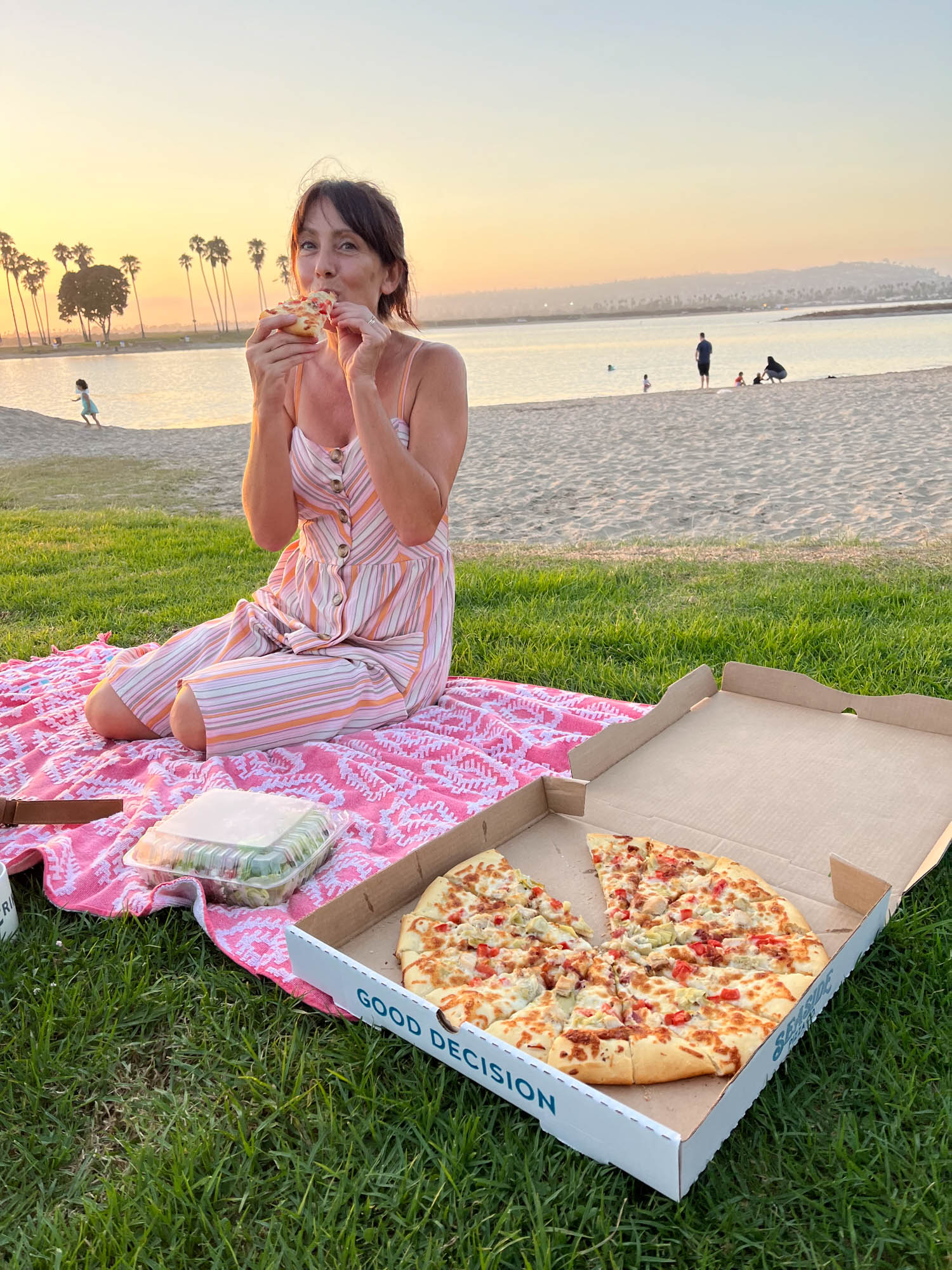 Outdoors, person sitting at the beach, enjoying a slice of take-away pizza