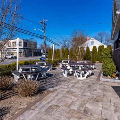 Outdoor seating area with picnic tables, surrounded by greenery, under a clear blue sky.