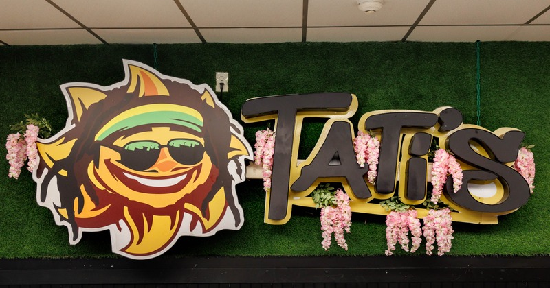 The sign for Tati's Island Cuisine on a greenery wall