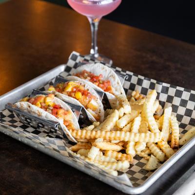 Fish Tacos served with crinkle-cut fries, alongside a cocktail.