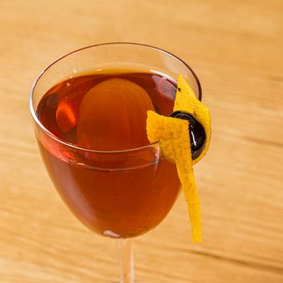 Manhattan cocktail served up with lemon peel and cherry garnish.