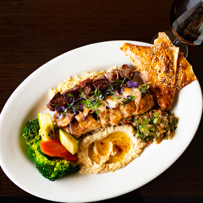 Plate with  beef, chicken, and shrimp skewers, pita, hummus, tabbouleh, and veggies.