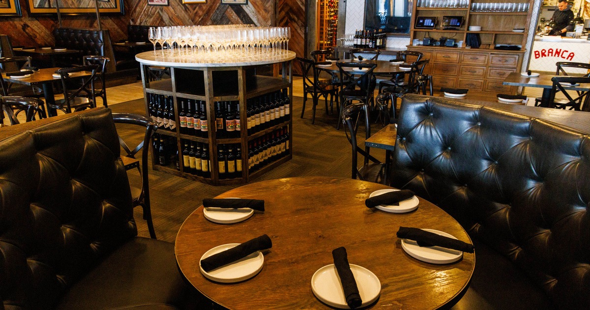 A restaurant interior with a round wooden table and black leather booth