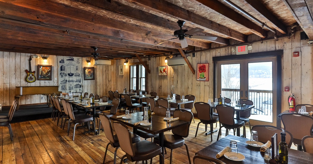Rustic restaurant interior with wooden floors, walls, and ceiling beams, set with tables and chairs