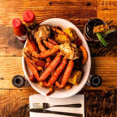 Seafood boil with crab, shrimp, corn on the cob, and a drink.