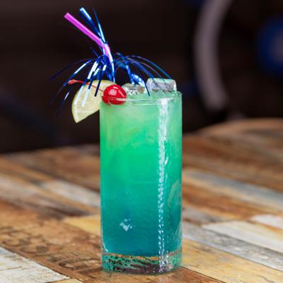 Blue green cocktail with lime wedge and cherry garnish.