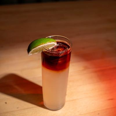 Dark N Stormy layered cocktail in a tall glass with lime garnish, set on a wooden table.