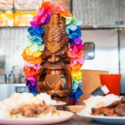 A wooden Tiki statue adorned with colorful leis, placed on a table with food plates.