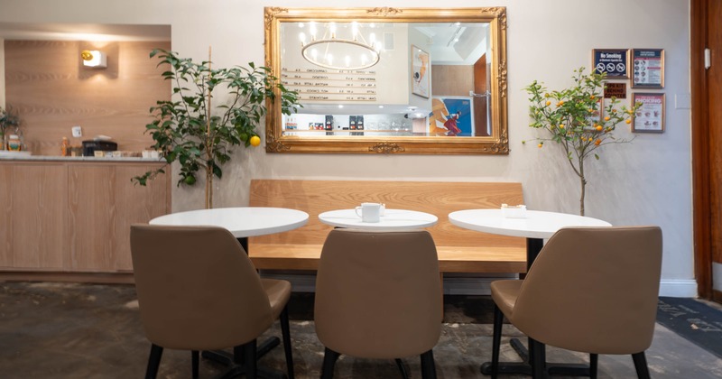 Cafe interior with tables, chairs, a large mirror, and potted citrus trees