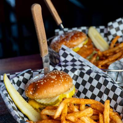 Sesame seed bun burgers with pickles and fries, in checkered baskets.