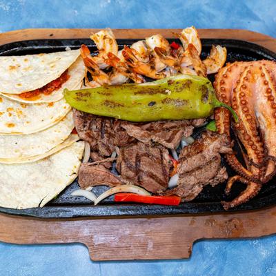 Surf and turf platter with grilled shrimp, steak, octopus, roasted pepper, and tacos.