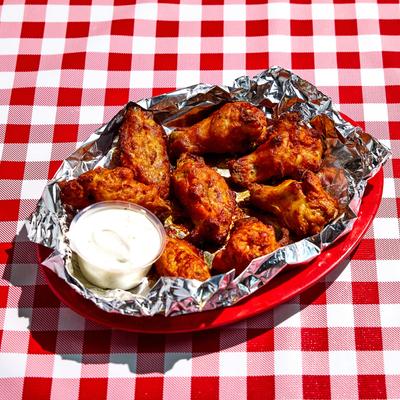 Chicken wings with dipping sauce on foil tray.