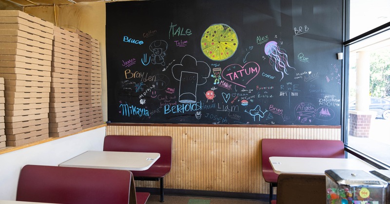 Restaurant interior with stacked pizza boxes, red booths, and a chalkboard wall
