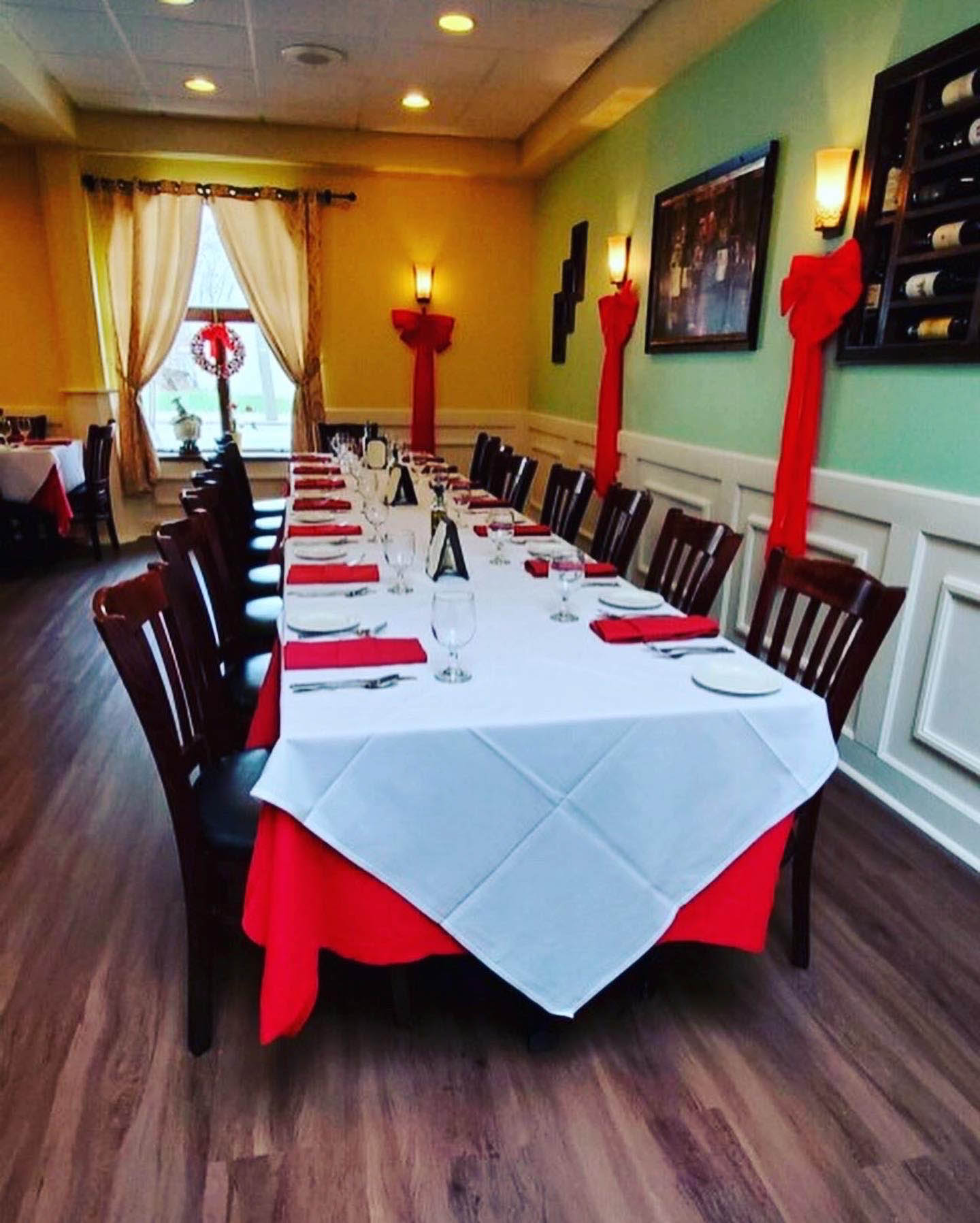 Long table set for dining, dark wood chairs, and decorative red accents