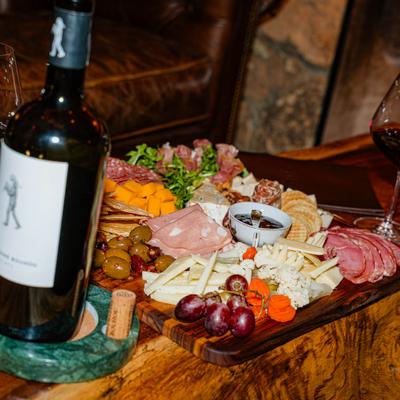 Charcuterie board on a wooden table with a wine bottle and glass.