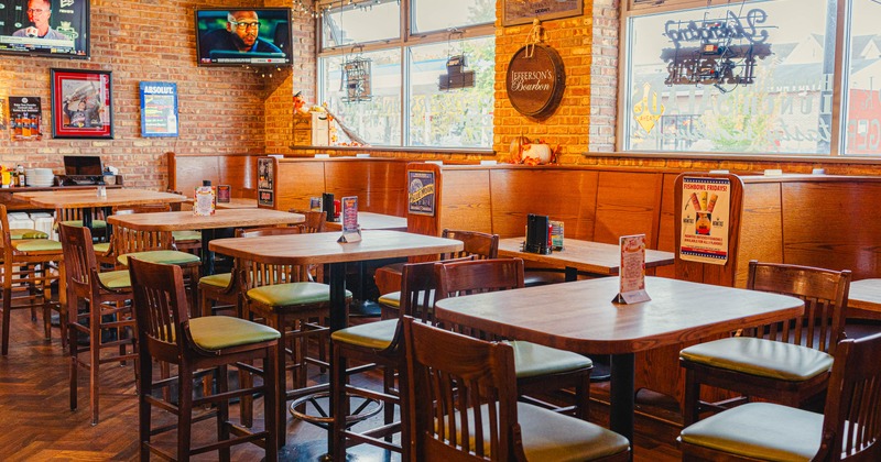 Interior of a restaurant with wooden tables and chairs, brick walls, and large windows