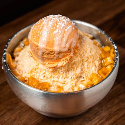 Mango bingsu  topped with a scoop of flavored ice cream and a drizzle of sauce.