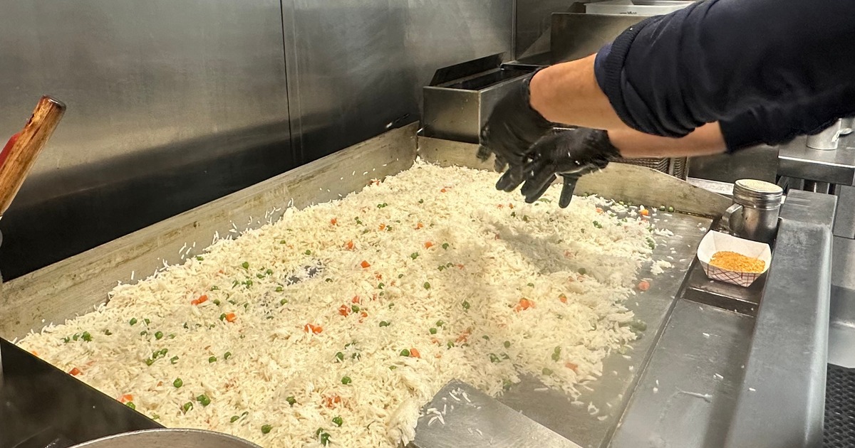 Gloved hands cooking rice on a flat grill