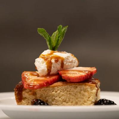 Tres leches cake featuring fresh strawberry toppings, whipped cream and a mint garnish.