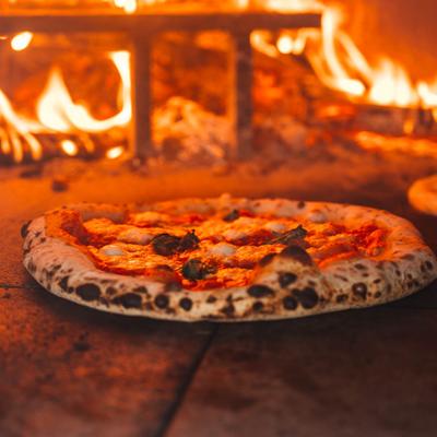 Margherita pizza cooking inside a wood-fired oven with visible flames..