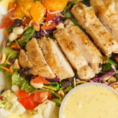 Salad with grilled chicken, mandarin oranges, peanut and a cup of dressing, close-up.