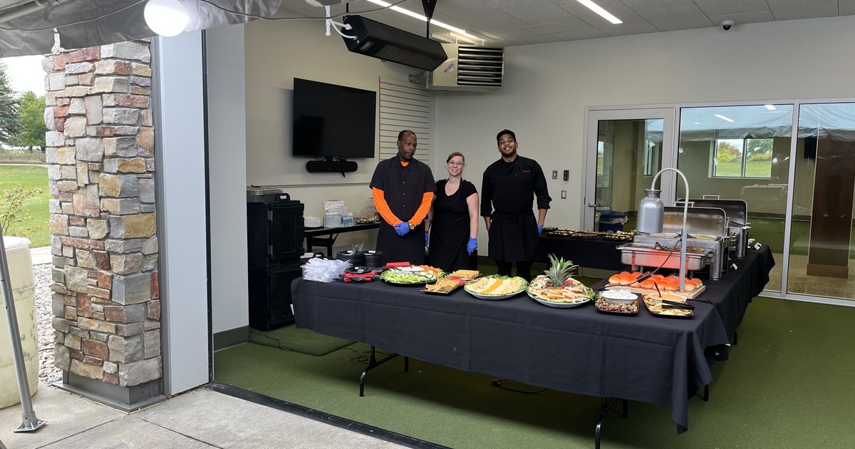 Catering table with prepared platters of food and staff posing behind it