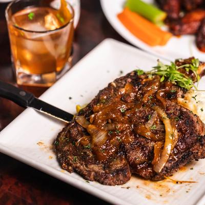 Grilled steak topped with caramelized onions served with mashed potatoes and a cocktail.