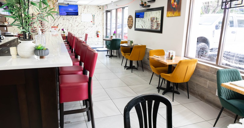Interior, bar with stools on the left, tables for two on the right, tile flooring