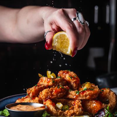 Hand squeezing lemon wedge over the plate of fried calamari.