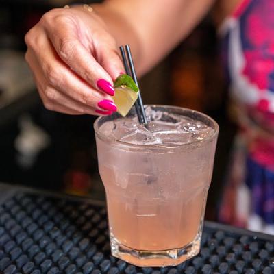 A bartender garnishes a glass of drink, close up on the glass on bar mat.