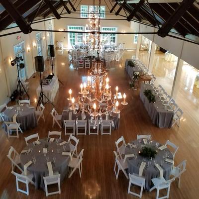 Elegant event venue with chandeliers, wooden floors, round tables, and banquet setup.