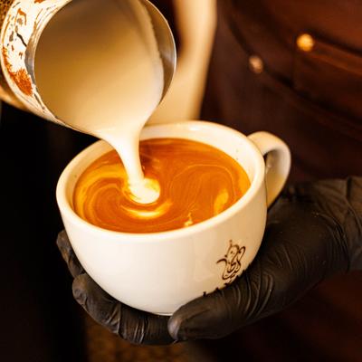 A barista pouring steamed milk into a cup of coffee to create latte art.
