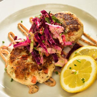 Blue Lump Crab Cakes with slaw on top, swirled sauce, and lemon slices.