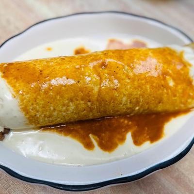 Wet burrito topped with a red salsa chili sauce and a white cheese sauce.