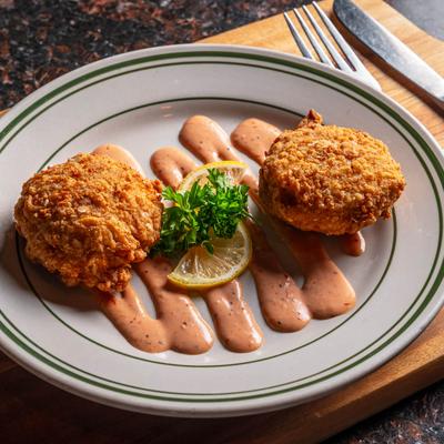 Two fried crab cakes served on a plate drizzled with a sauce