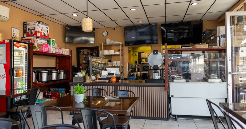 Interior view of a cozy cafe with a service counter, and dark tables with chairs