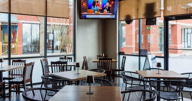 Empty restaurant seating area with large windows and television